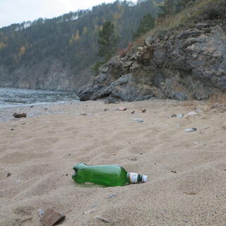 A clear green beer bottle on a sandy beach.