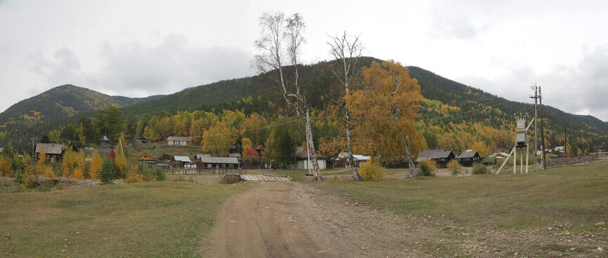 Wooden houses surrounded by forest, and in the background, a large hill.
