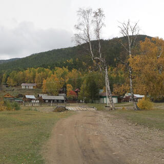 Wooden houses surrounded by forest, and in the background, a large hill.