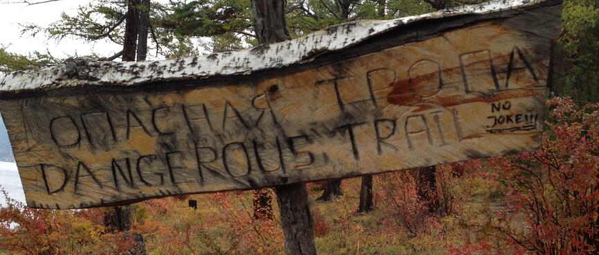 A bilingual homemade sign reads 'DANGEROUS TRAIL'.