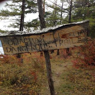 A bilingual homemade sign reads 'DANGEROUS TRAIL'.