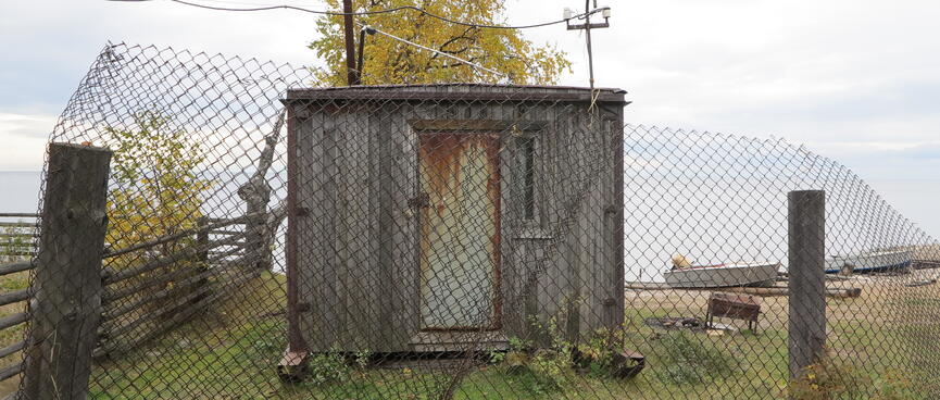 A rusty hut behind a wire mesh fence.