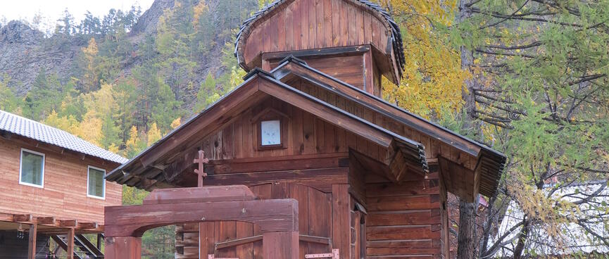 A very small wooden church sits behind a tall wooden gate.