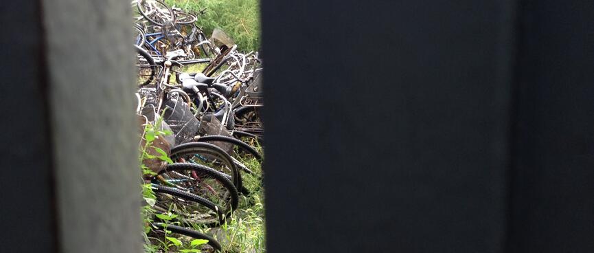 A slit in a gate reveals a pile of old bicycles.