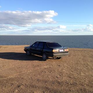 A black car parked on a barren, elevated section of the shore.