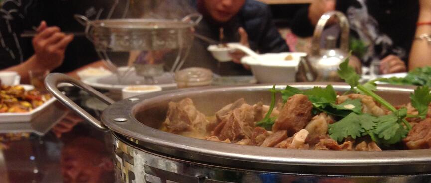 People eat after serving themselves from a heated metal dish filled with meat.
