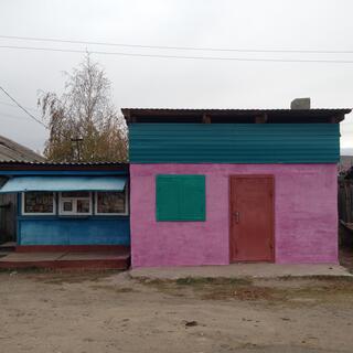 A small building is painted pink, with a red door and green shutters over the window.