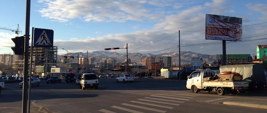 Views of apartment buildings and snowy mountains at a busy intersection.