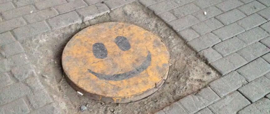 A manhole cover is painted with a yellow smiley face.