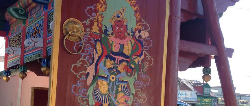An ornate wooden painting of a dark skinned god wearing a pink scarf.
