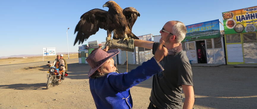 A lady in a blue cloak and brown hat waves her arms to scare the eagle.