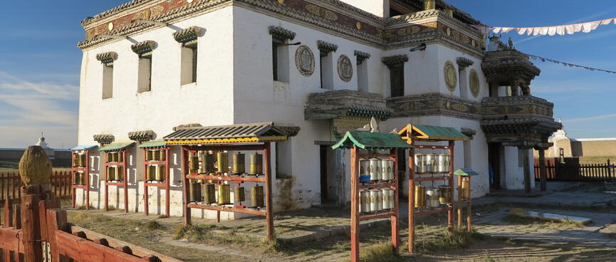 Prayer wheels and flags outside a two story stone building.