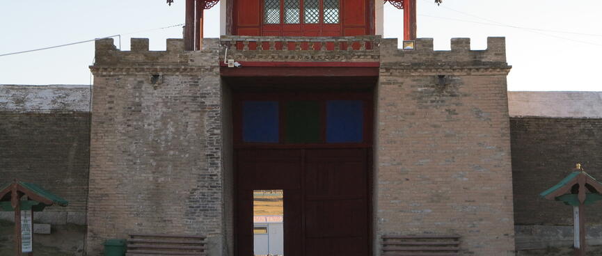 A small red building sits on top of a tall stone battlement containing a doorway.