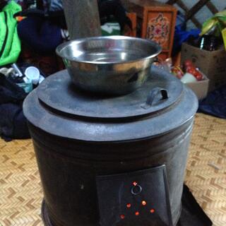 A bowl of water sits on top of a round stove containing a fire.