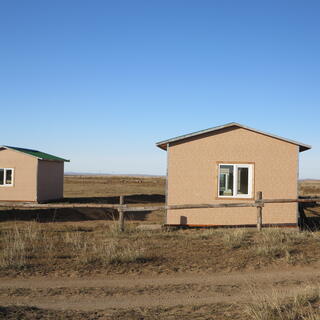 Identical windowed huts, light brown with green roofs.