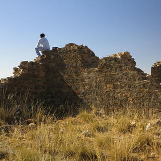 A man sits on top of derelict stone walls.