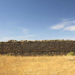 A stone wall separates the blue sky from the dry yellow grass.