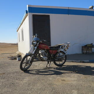 A red Dayun motorcycle parked outside a square white building with blue trim.