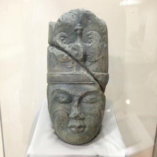 Carved stone head with closed eyes wearing a tall ceremonial headdress.