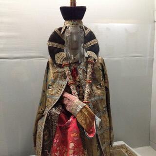 A mannequin in gold and red ceremonial robes has her hair tied in a loop.