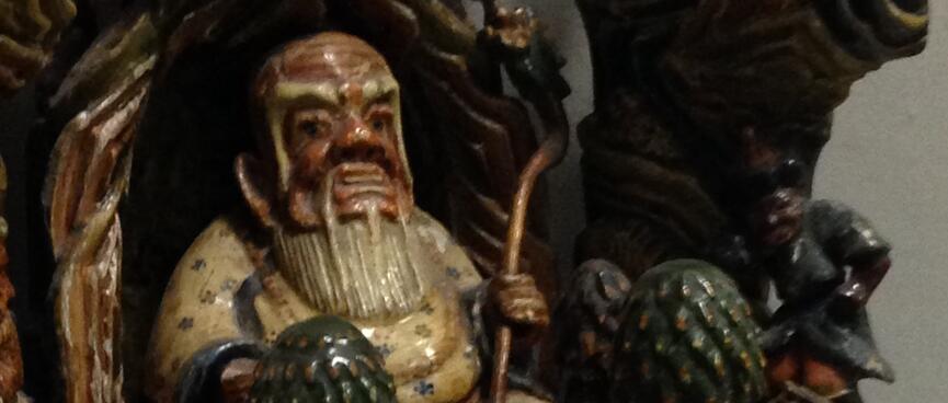 A shiny painted wooden statue showing a fat man with a white beard sitting in a doorway.