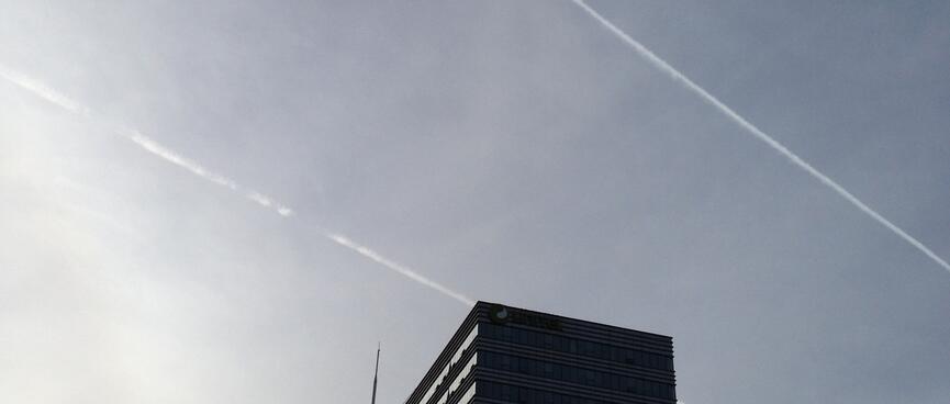 Twin vapour trails in the blue skies above an office block.