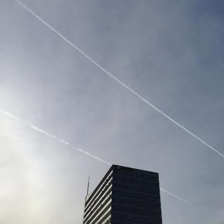 Twin vapour trails in the blue skies above an office block.