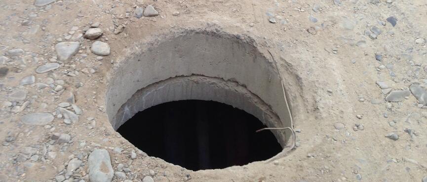 A uncovered manhole in the middle of a narrow unpaved street.