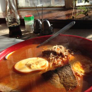 Sunlight fills a red bowl containing a hearty broth.