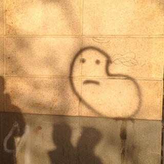 Shadows of people and graffiti of an unidentified creature on a brick wall.