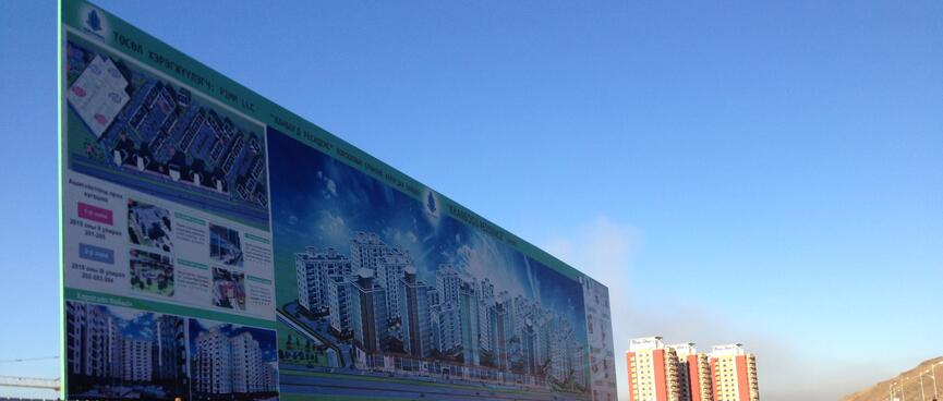 A large billboard for a new housing development depicts a concentrated cluster of tall apartment blocks.