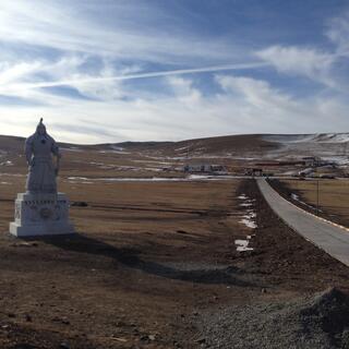 A statue of Genghis Khan next to a thin ashphalt road.