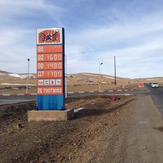 A tall orange sign with prices for four types of fuel.