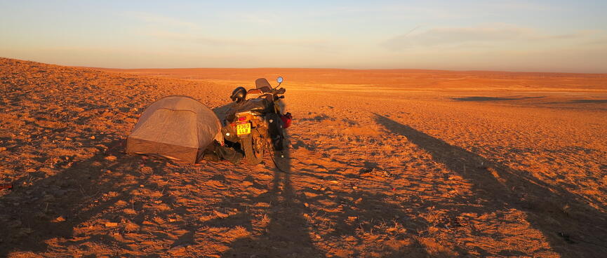 Tall shadows either side of a tent and a motorbike.