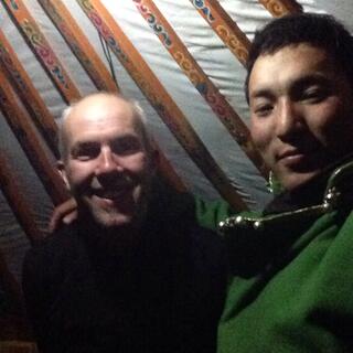 Photo with one of the brothers. He is wearing a long green coat and behind us are the patterned slats of the ger roof.
