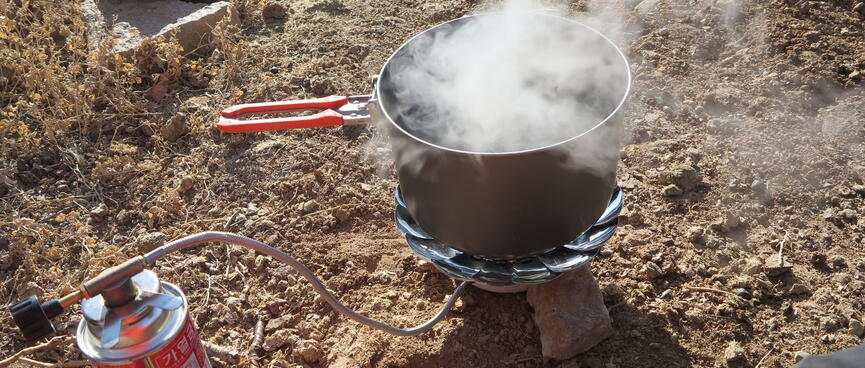 A steaming pot on top of a metal gas cooking stove.