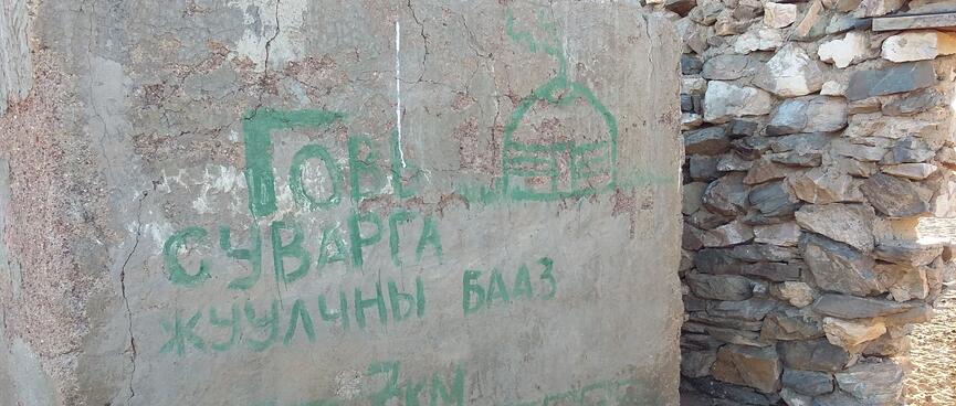 A concrete wall contains a painted message and a picture of a dome, which is presumably a ger.