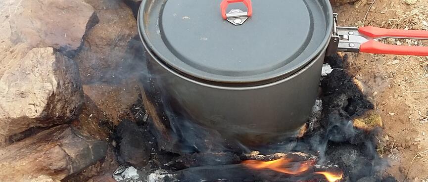 A camping pot sits on top of a pile of flaming animal dung.