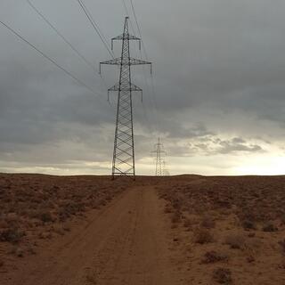 A line of power pylons next to a sandy path.