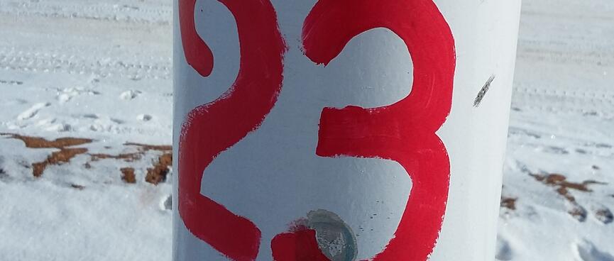 The number 23 is hand painted in red on a white pole.