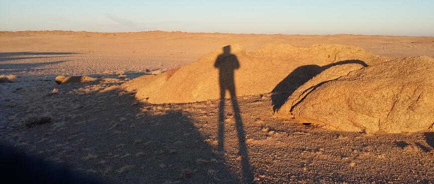 My elongated shadow contrasts against sand and light brown boulders.