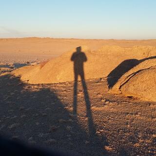 My elongated shadow contrasts against sand and light brown boulders.