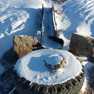 A snow covered tyre lies at the top of a rise, A metal trough sits below.