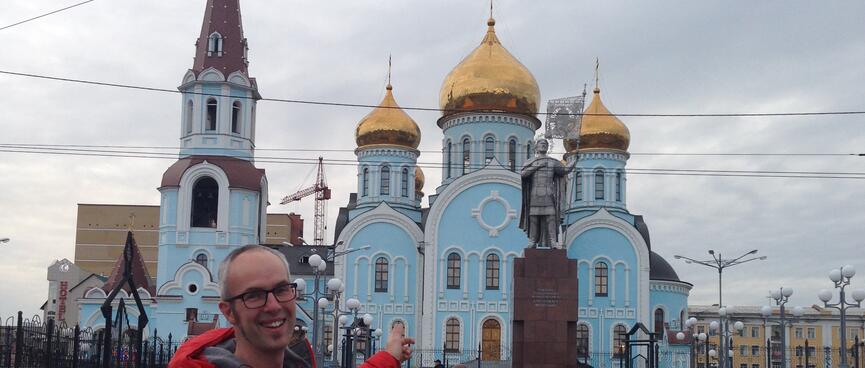 A pale blue four story church with golden onion domes and a tall tower, opposite Chitaʼs Railway Station.