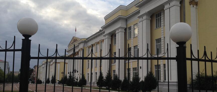 Four story yellow buildings with white rectangular columns sit behind tall metal gates, in Chita.