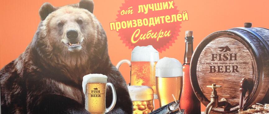 A large brown bear holds a large glass of beer between his paws.
