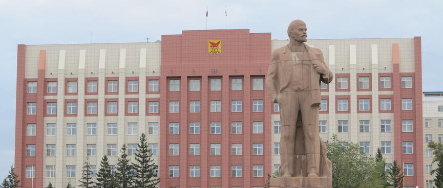 A large statue of Lenin, on a pedestal outside an eight story building with many windows, in Chita.