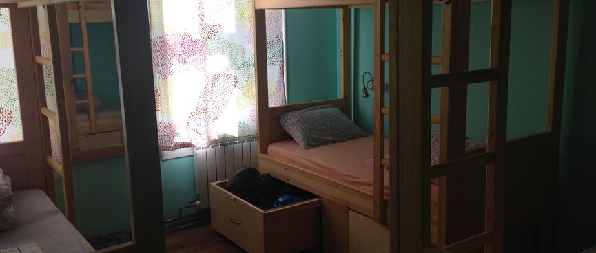 A room of bunks is partially illuminated by thin floral curtains.