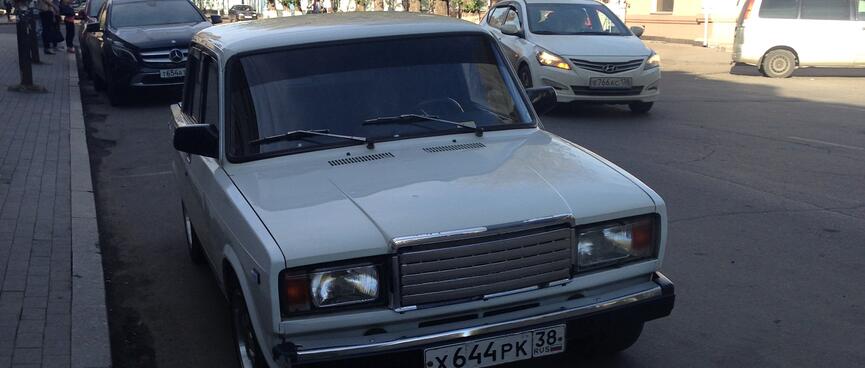 A shiny white Lada is parked on a side street.