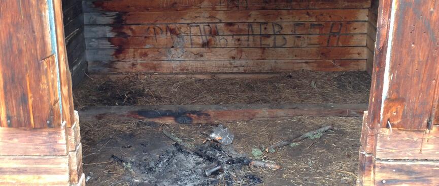 A pile of ashes, and black writing on wooden walls.